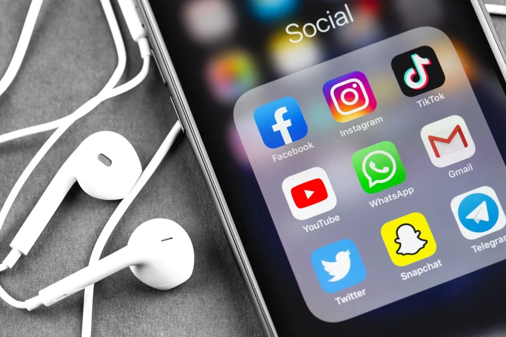 social media icons on a phone menu with earbuds sitting next to the phone