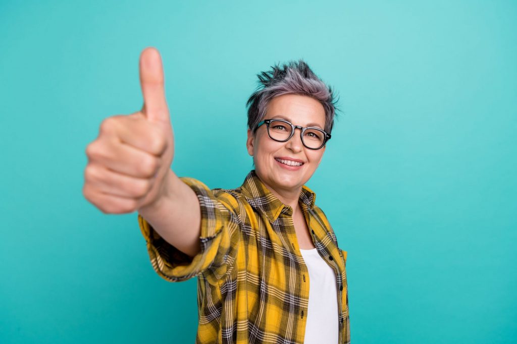 older lady with glasses and yellow flannel shirt making a thumbs up for the camera