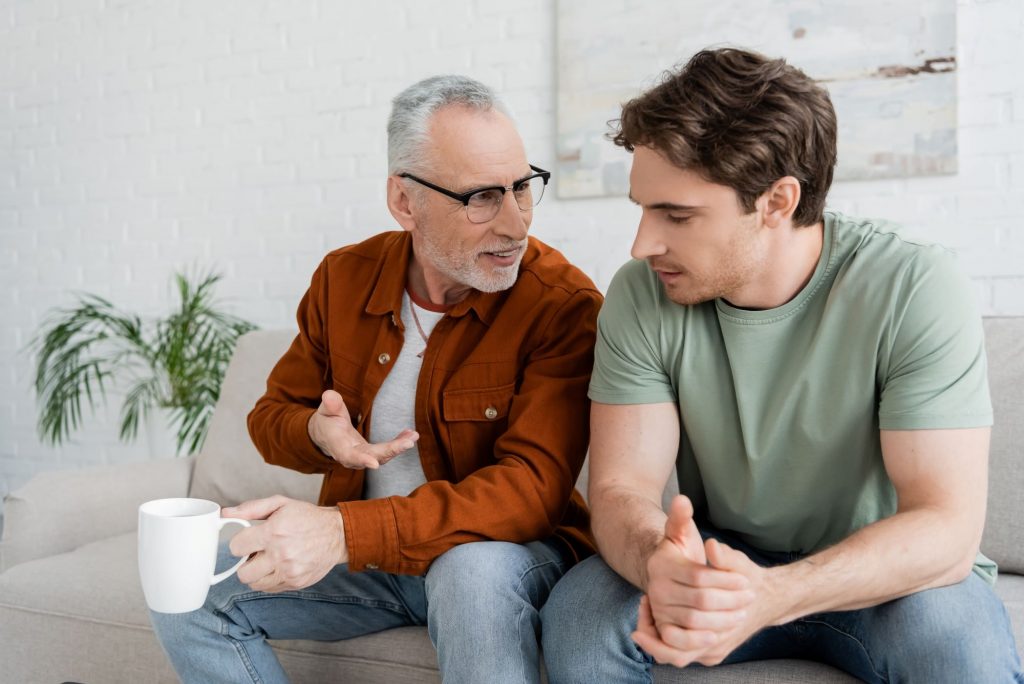 adult son and father sitting on the couch having a discussion