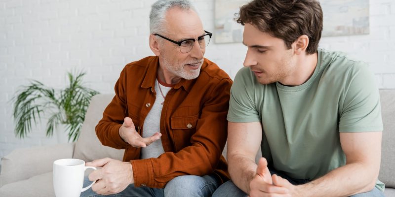 adult son and father sitting on the couch having a discussion