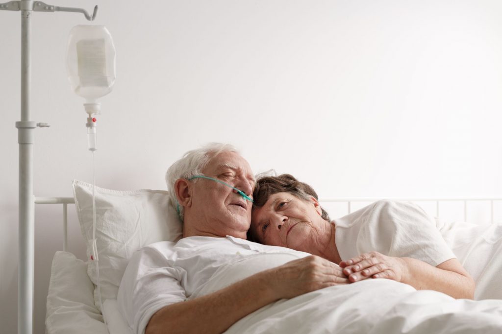 senior wife laying in bed with dying husband during end-of-life care in hospice