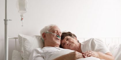 senior wife laying in bed with dying husband during end-of-life care in hospice