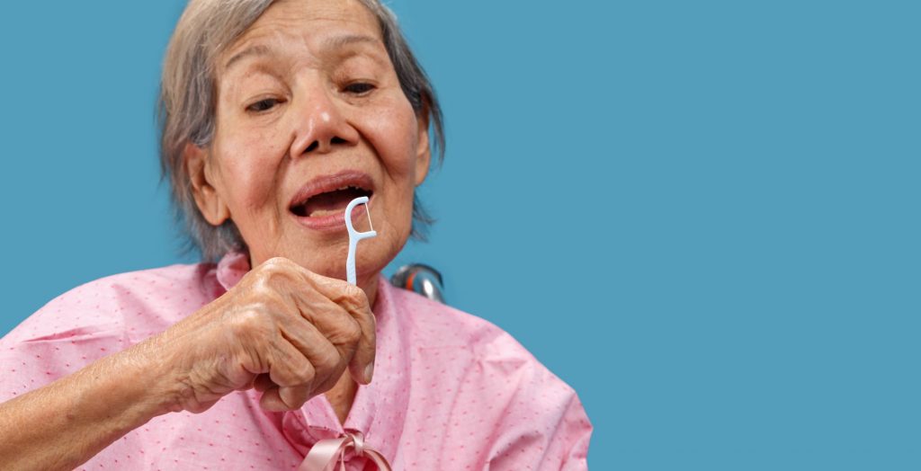 elderly Asain woman in a wheelchair using a dental floss picker