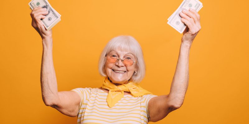 a healthy and wealthy senior woman holding money and smiling with orange background