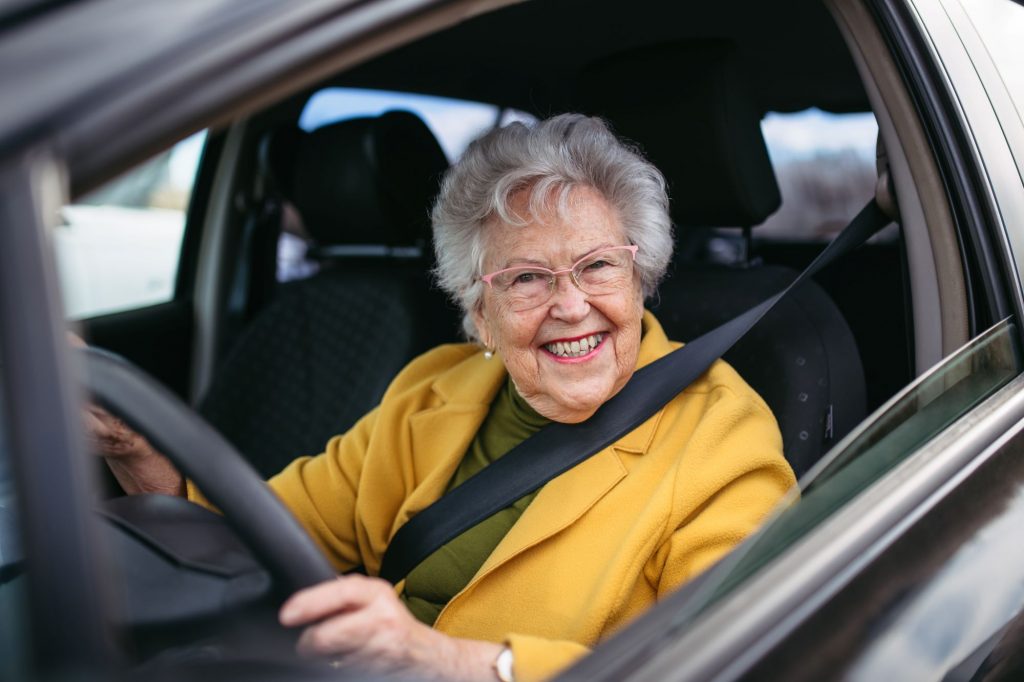 older senior woman driver smiling while holding the steering wheel