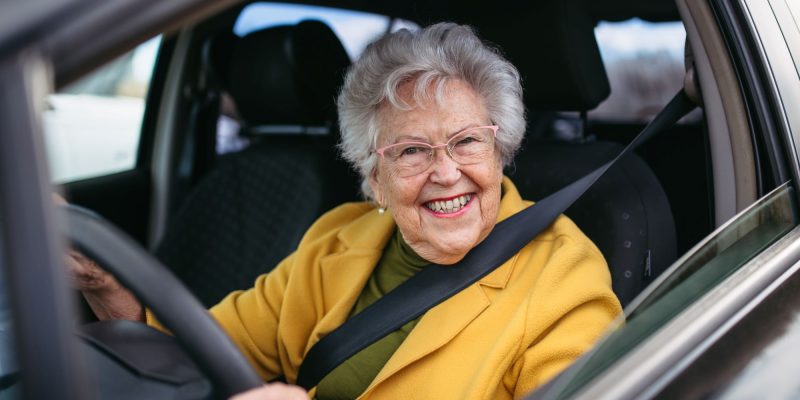 older senior woman driver smiling while holding the steering wheel