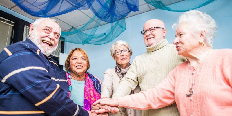 group of smiling and happy seniors, male and female, in an adult day care or adult day health care setting, blue streamers hanging from ceiling above