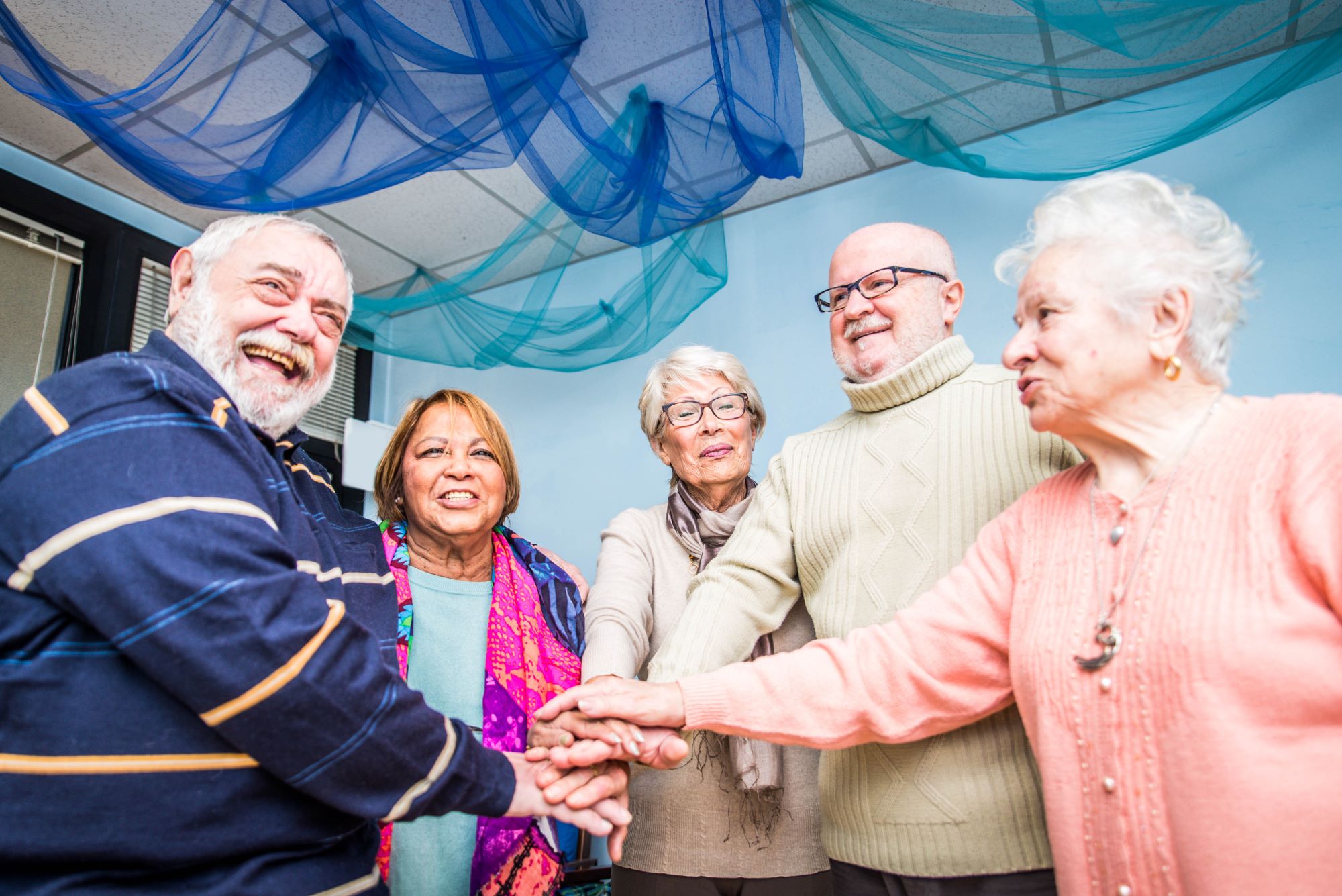 group of smiling and happy seniors, male and female, in an adult day care or adult day health care setting, blue streamers hanging from ceiling above