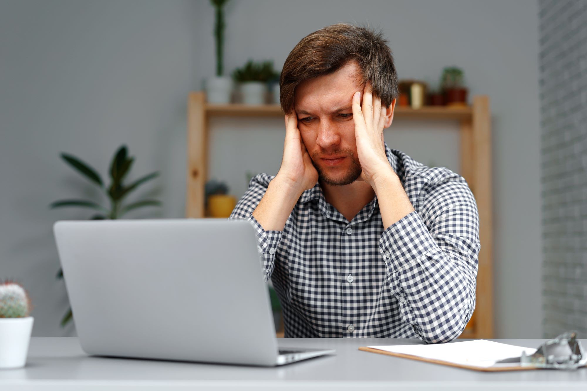 distressed man in front of computer holding head Son Loses Mom's House Because of Poor Medicaid Choices