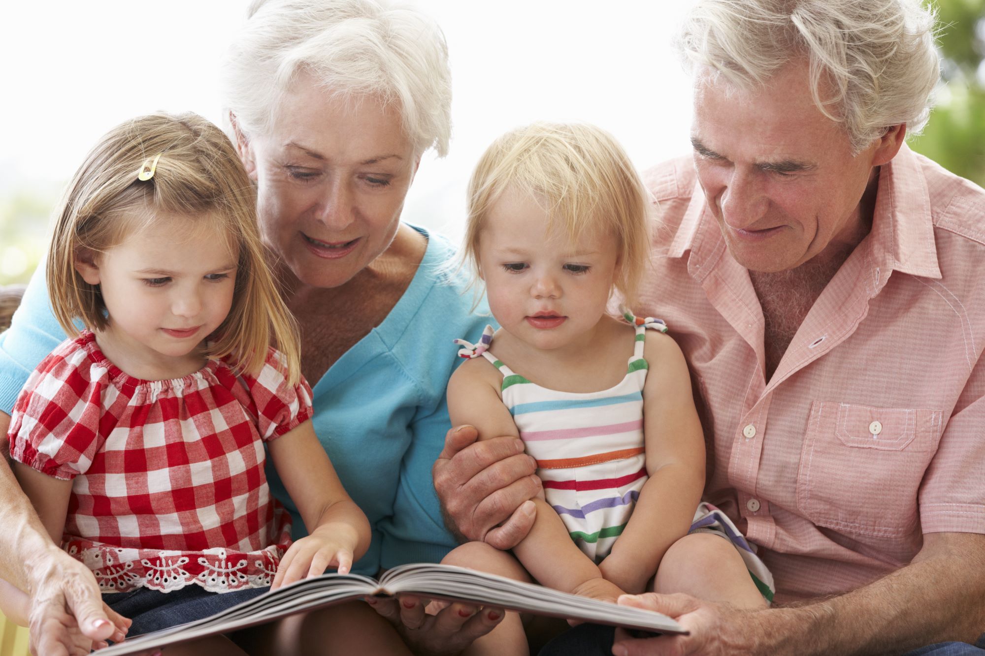young grandchildren with grandparents reading a book