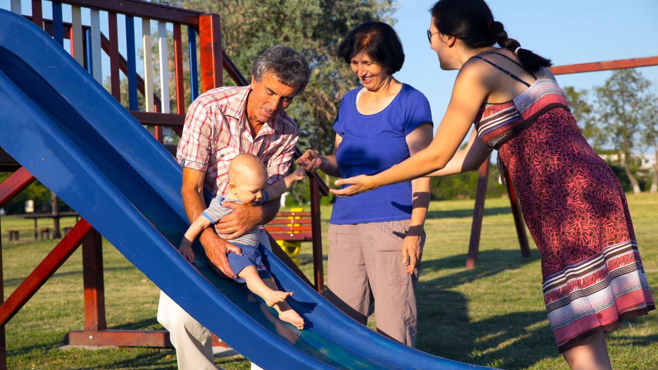 grandparents and adult child at the playground with grandchild