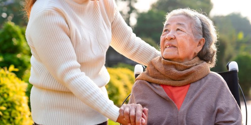 Asain senior in a wheelchair, looking up and talking to a woman loved one or caregiver