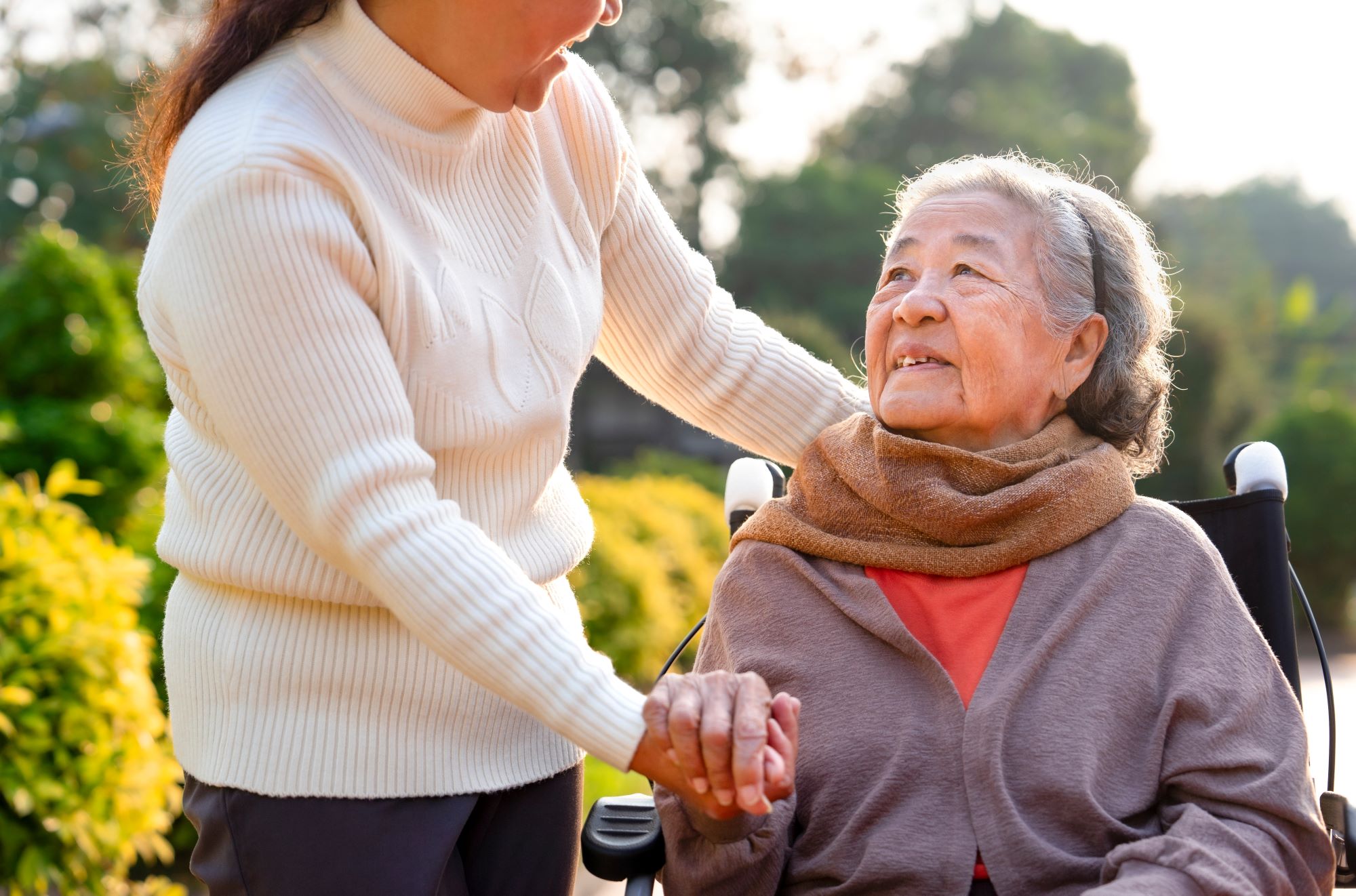 Asain senior in a wheelchair, looking up and talking to a woman loved one or caregiver