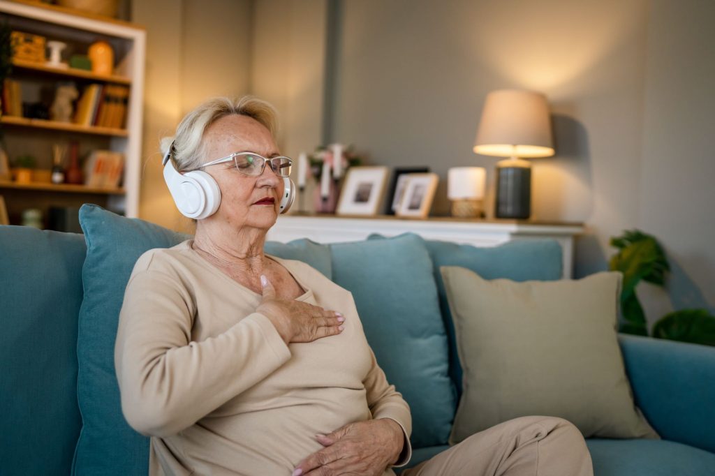 senior woman sitting on couching listening to headphones and beathing deep