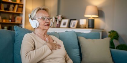 senior woman sitting on couching listening to headphones and beathing deep
