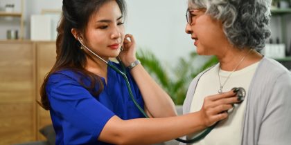 Asain home care helper using stethescope on Asain senior woman with short, curly gray hair