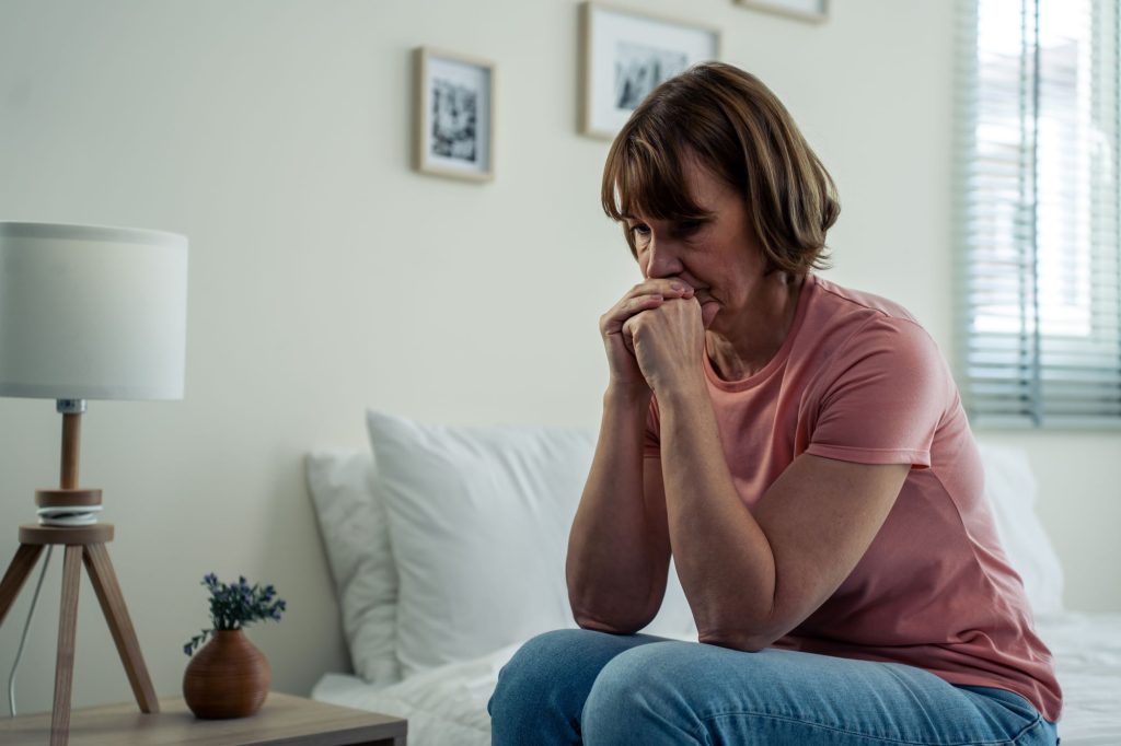 older retiree woman sitting on the bed with a sad, lonely, forgotten look on her face