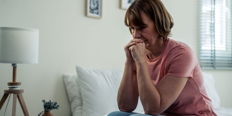 older retiree woman sitting on the bed with a sad, lonely, forgotten look on her face