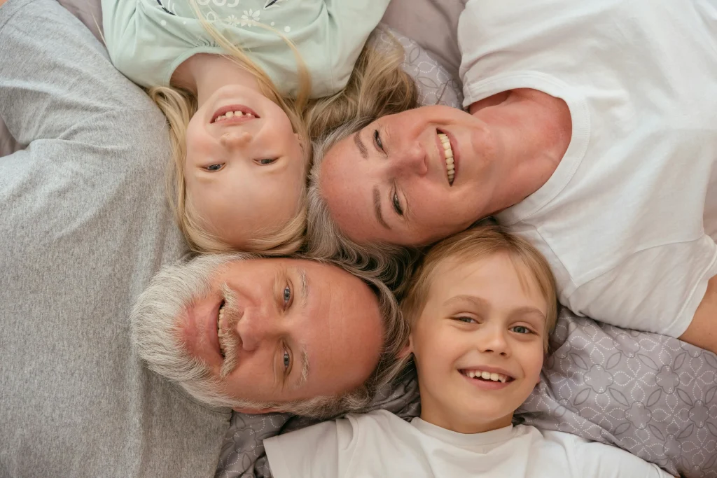grandparents and grandchildren lying on bed together smiling up at camera