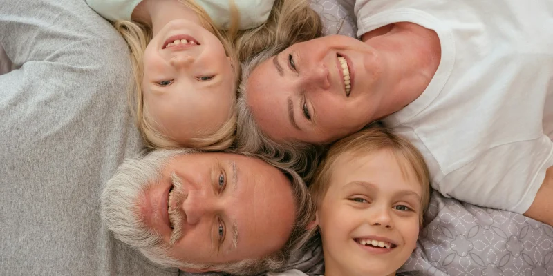 grandparents and grandchildren lying on bed together smiling up at camera