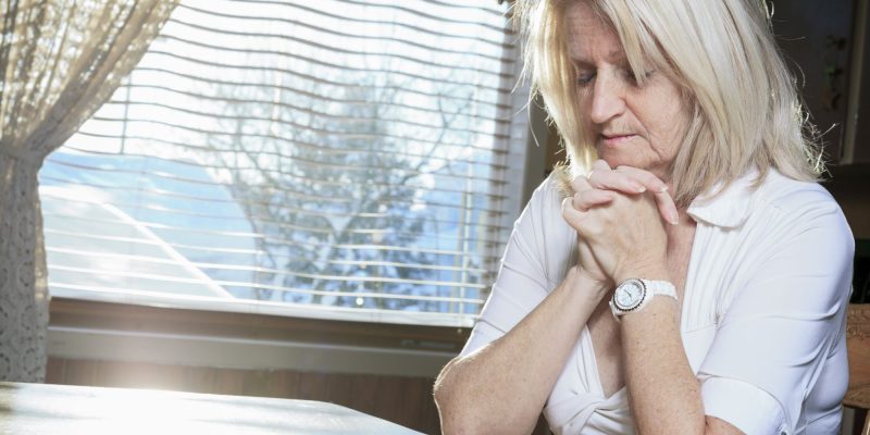 senior, retiree woman folding hands in prayer at the kitchen table