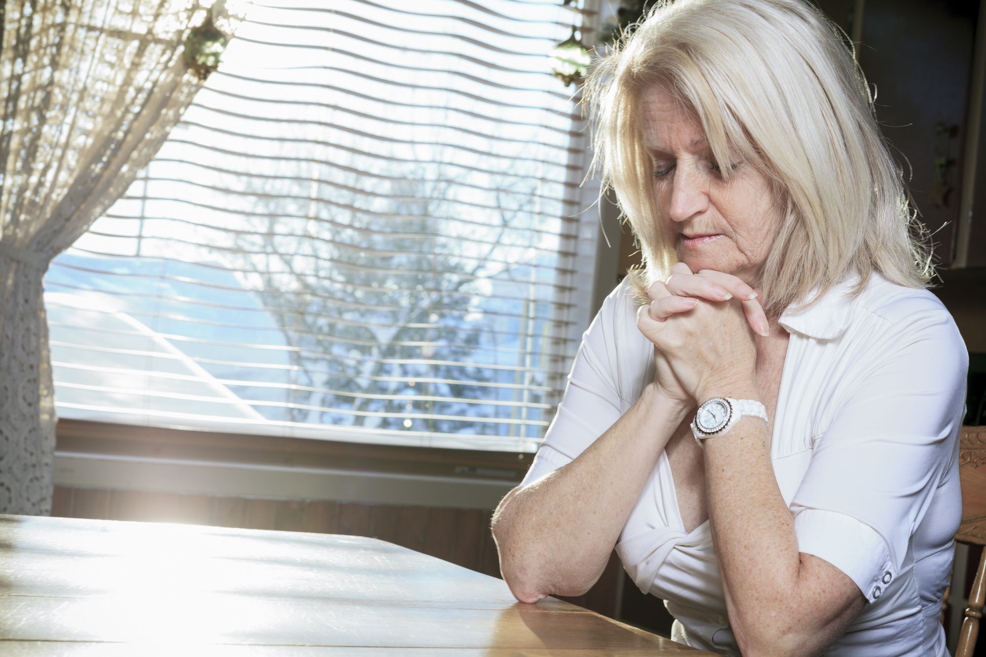 senior, retiree woman folding hands in prayer at the kitchen table