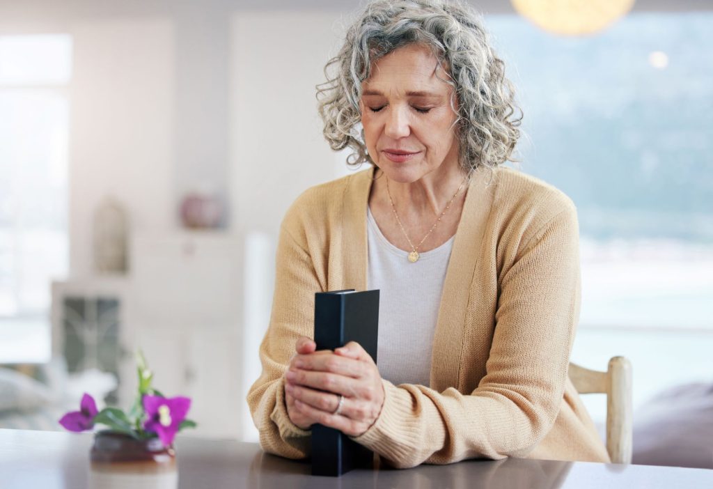 praying senior woman sitting at table with bible and flowers