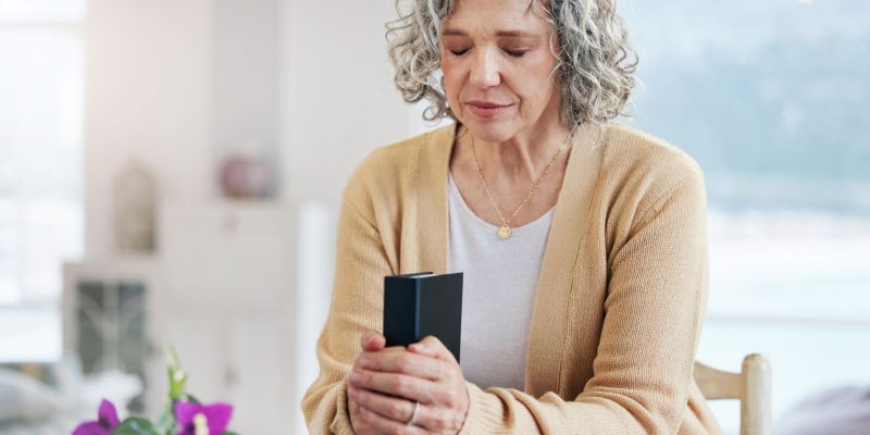 praying senior woman sitting at table with bible and flowers