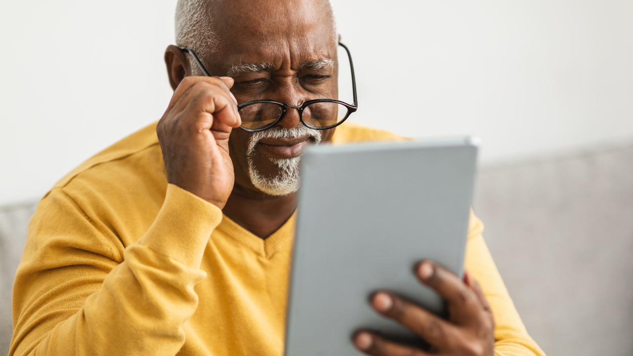 african american senior reading tablet with glasses and yellow shirt