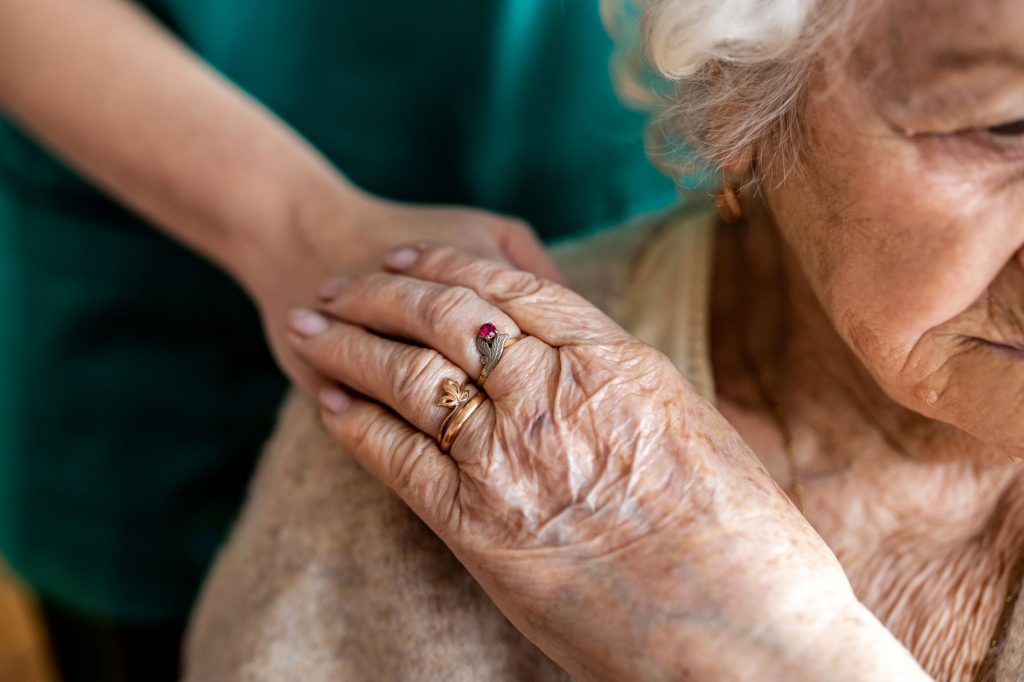 senior woman holding hands with caregiver standing behind her