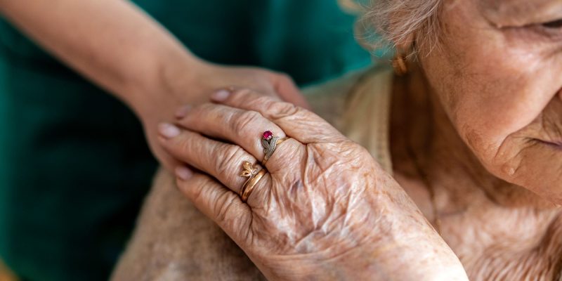 senior woman holding hands with caregiver standing behind her