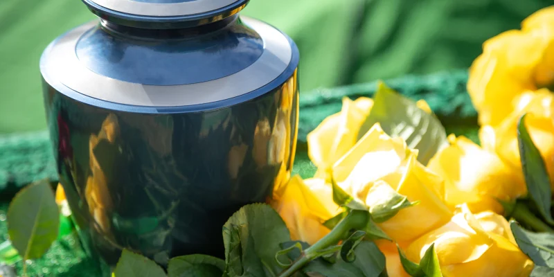 Close up on a burial urn with yellow roses, in a bright funeral scene