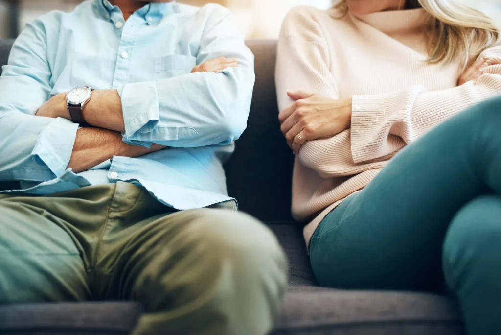 Angry couple with arms crossed sitting on couch, maybe fighting about money, financial problems