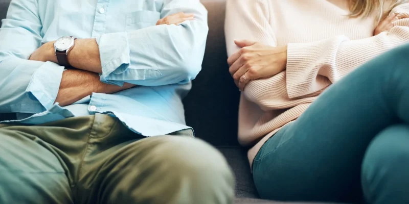 Angry couple with arms crossed sitting on couch, maybe fighting about money, financial problems