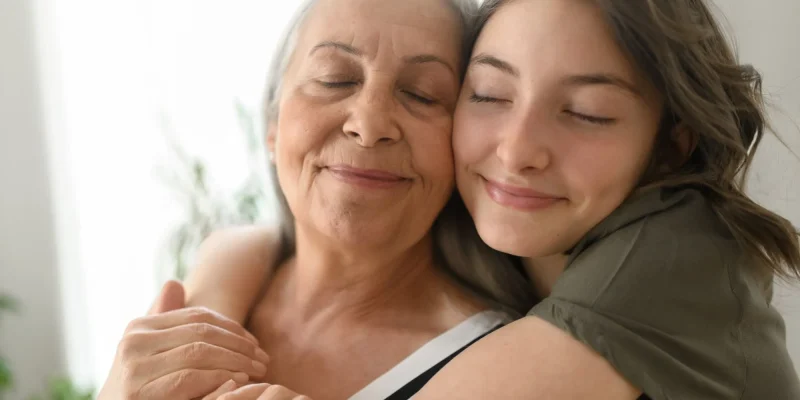 Senior grandmother with teenage granddaguhter hugging together at home.