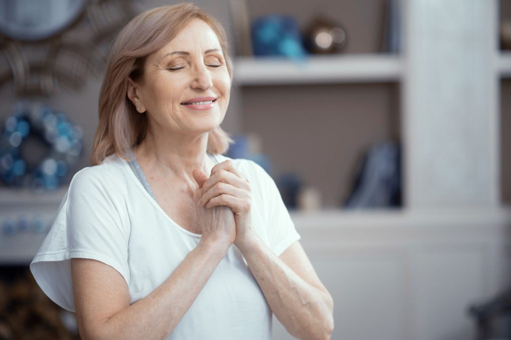 Happy Woman Is Pressing Her Arms To The Chest. Satisfied Woman With Closed Eyes Smiles And Presses Hands To The Chest. Portrait. Woman In Prayer Pose.