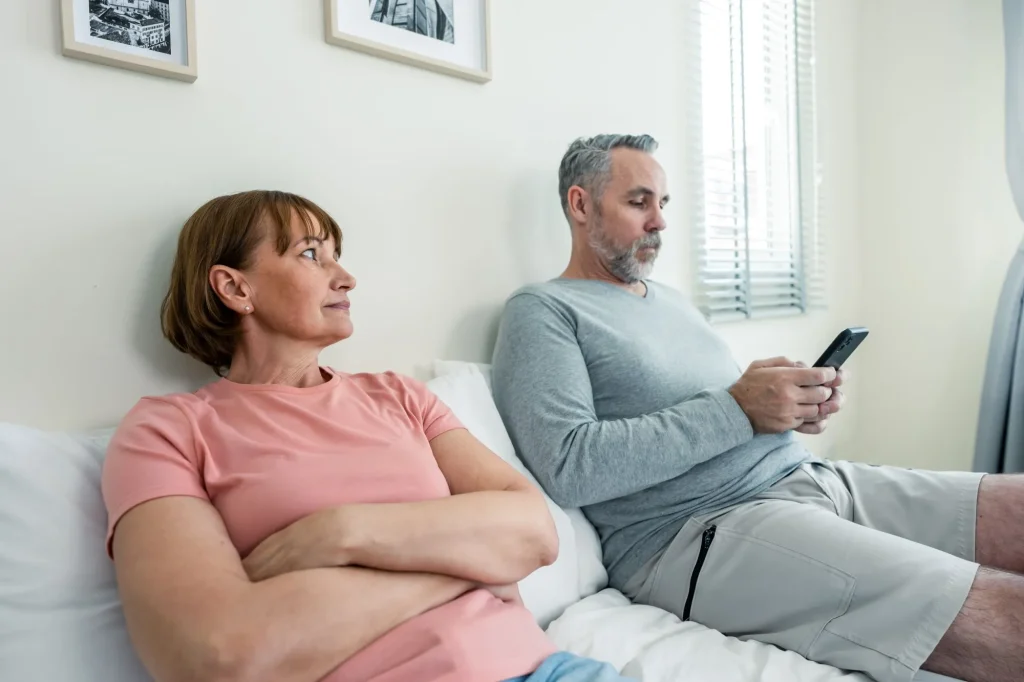 Phone addiction, Caucasian husband doesn't pay attention to his wife. Family problem-separation, Senior elderly mature couple sitting on bed and using smartphone, ignore each other in bedroom at home.