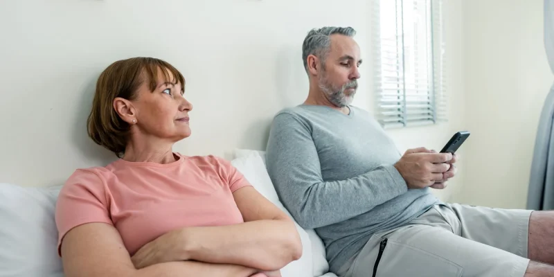 Phone addiction, Caucasian husband doesn't pay attention to his wife. Family problem-separation, Senior elderly mature couple sitting on bed and using smartphone, ignore each other in bedroom at home.