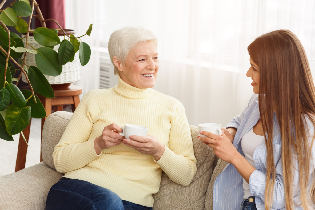 senior mother and adult daughter talking on the couch with coffee in their hands