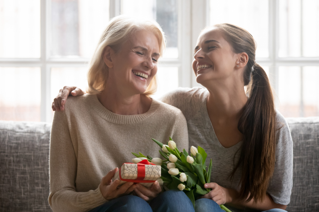 mom and daughter with gifts and flowers, laughing together on couch