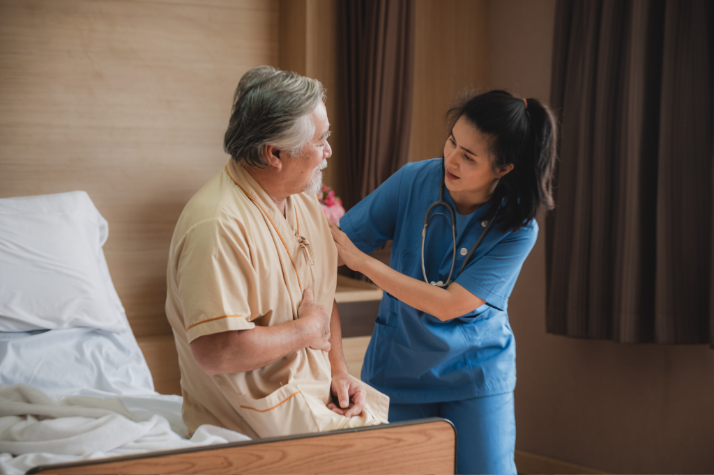 older asian gentleman sitting on a bed as a younger asian nurse assists him