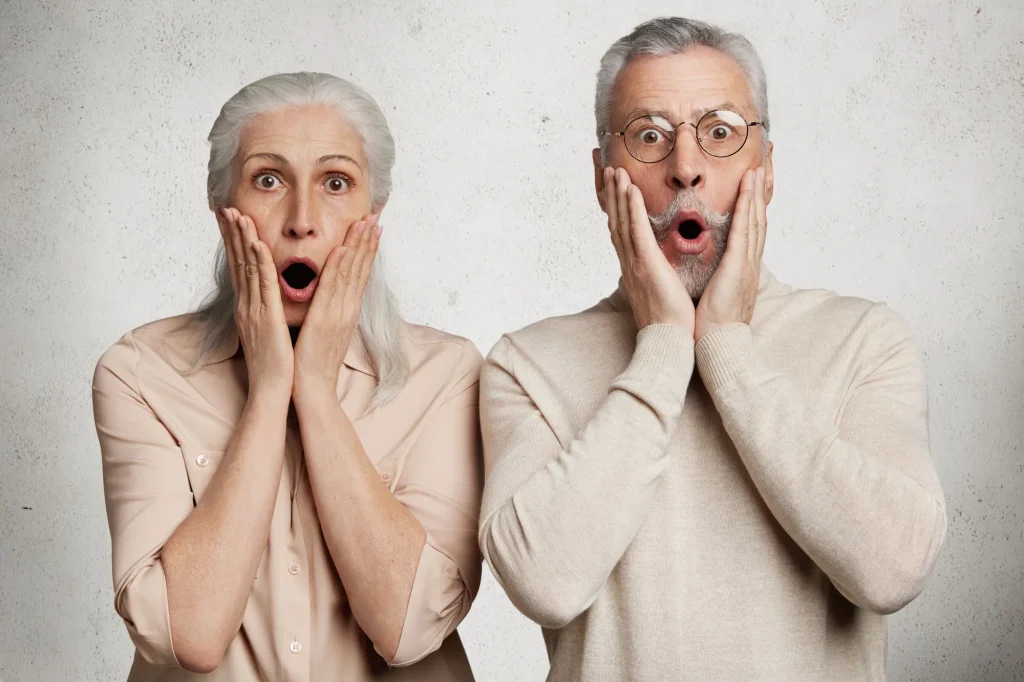 Elderly female and male stare at camera with terrified expressions, realize that they can`t pay bills, live only on pension, have financial crisis, isolated on white background. OLd couple in trouble