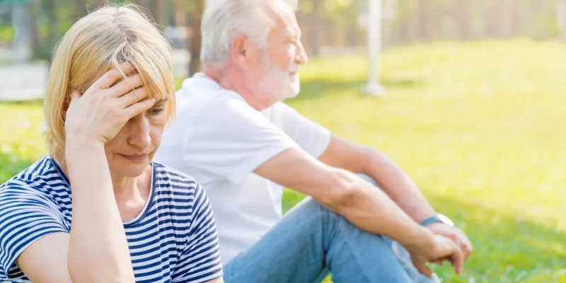 senior couple sitting outisde, arguing with one another, not speaking