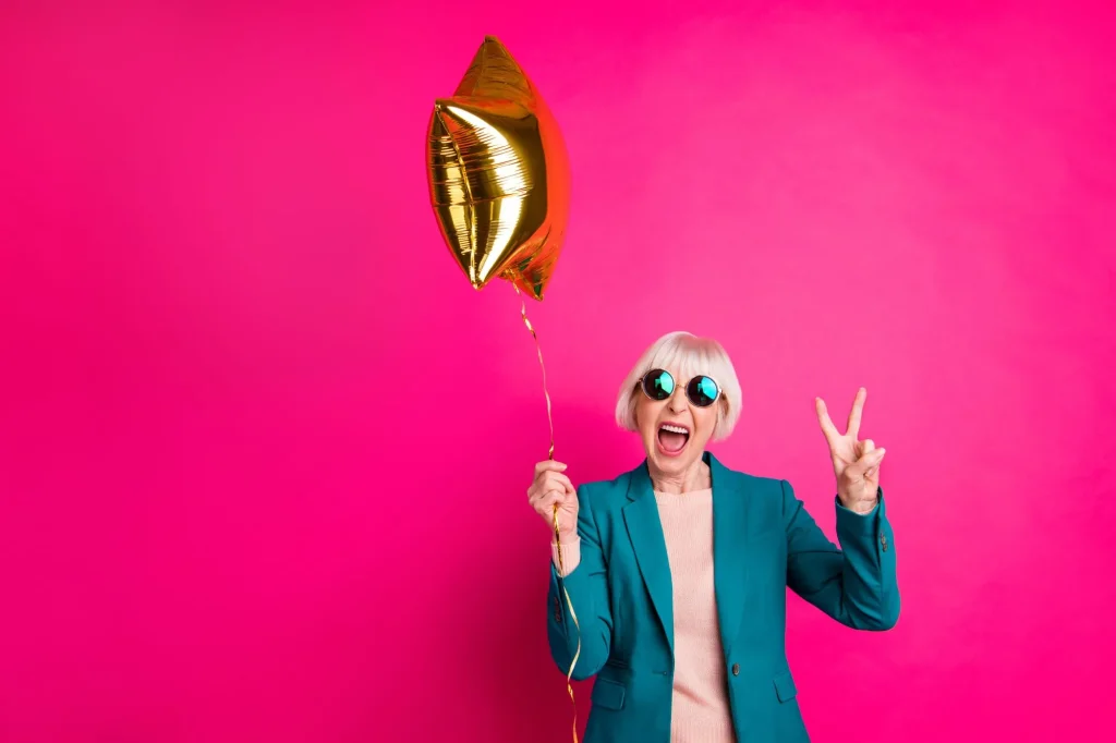 Portrait of her she nice-looking attractive crazy overjoyed cheerful cheery gray-haired lady holding balloon showing v-sign isolated on bright vivid shine vibrant pink fuchsia color background