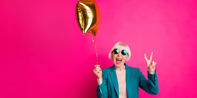 Portrait of her she nice-looking attractive crazy overjoyed cheerful cheery gray-haired lady holding balloon showing v-sign isolated on bright vivid shine vibrant pink fuchsia color background