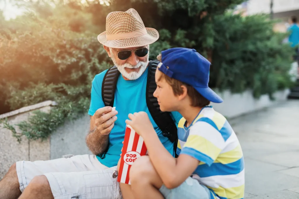 Happy grandfather enjoying with his grandson while eating popcorn outdoors in city street.