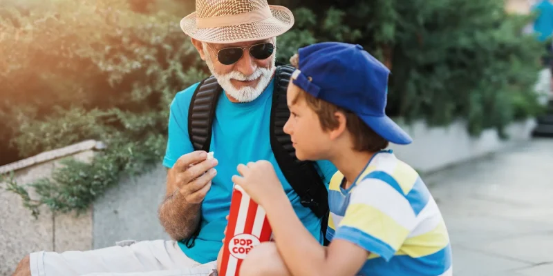 Happy grandfather enjoying with his grandson while eating popcorn outdoors in city street.