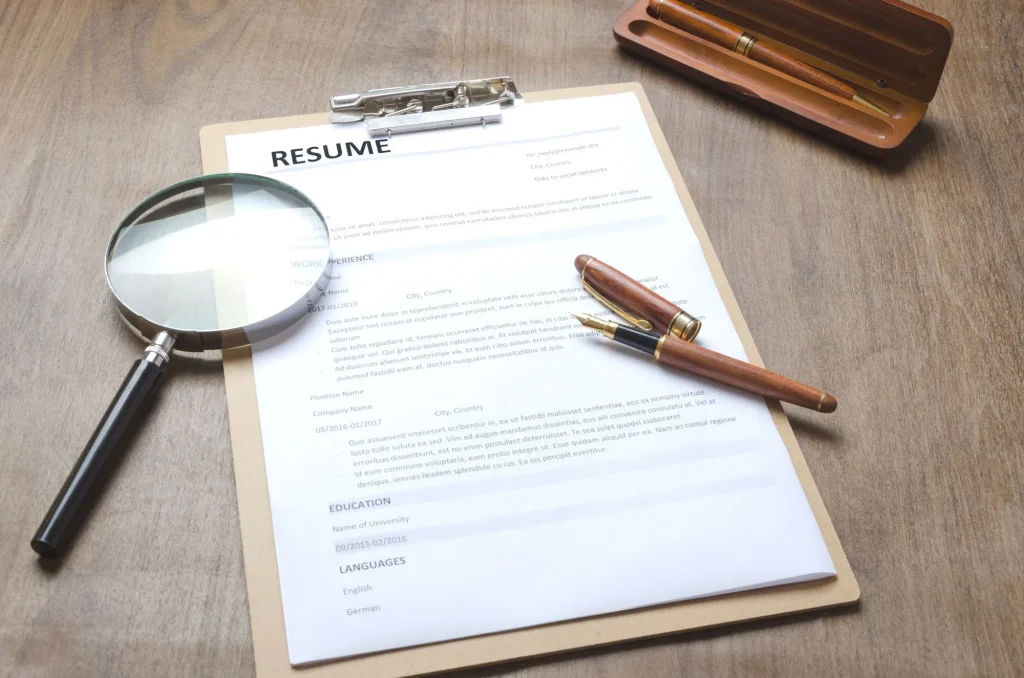 Closeup of a resume application,clipboard,pen, magnifier on wooden table,working process-hiring new people.Concept of hiring new employee with professional skills