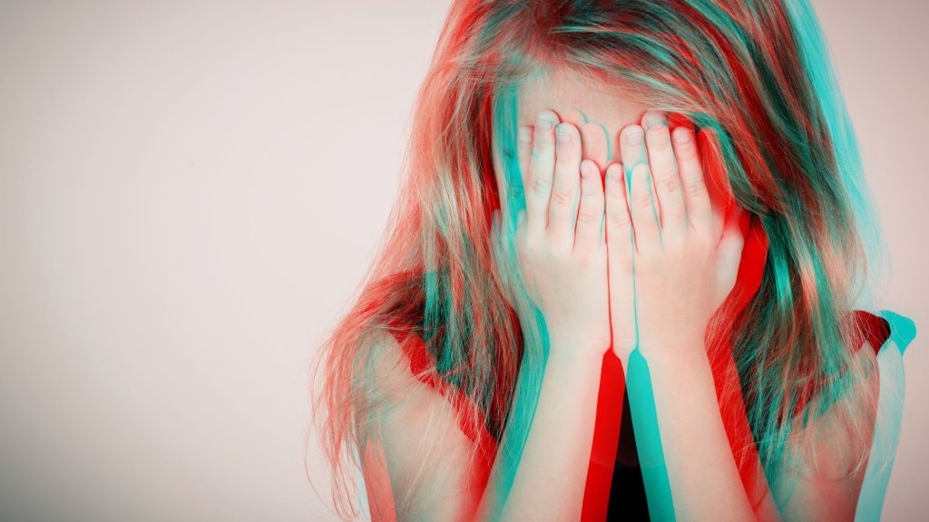 Portrait of sad blond little girl sitting outdoors near a wall at the day time. Concept of sadness. Glitched style photo.