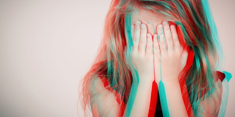 Portrait of sad blond little girl sitting outdoors near a wall at the day time. Concept of sadness. Glitched style photo.